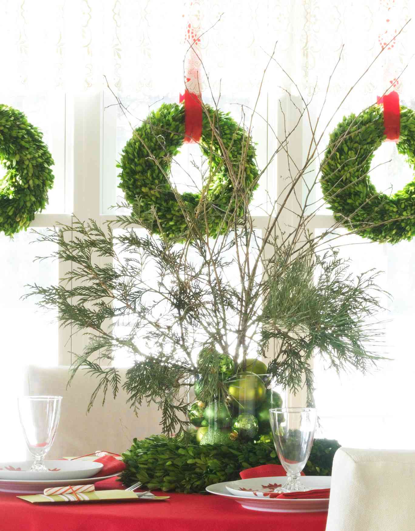 Bright green ornaments sit in a clear container on top of a wreath as a Christmas centerpiece